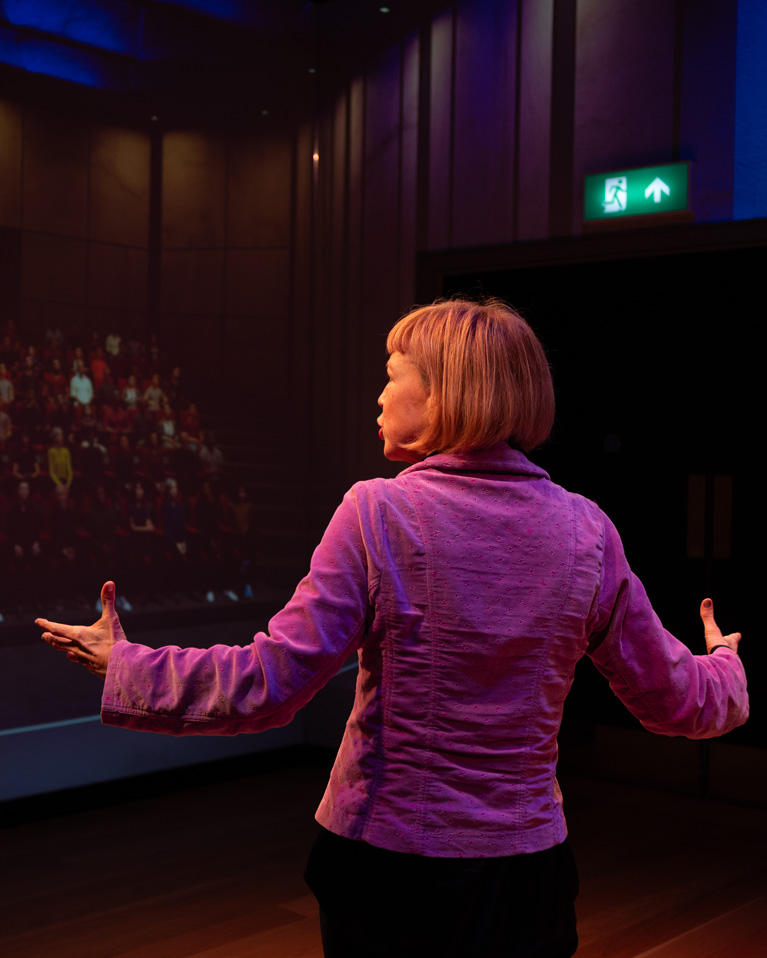 A women wearing a purple blazer, speaking to a virtual audience simulated.